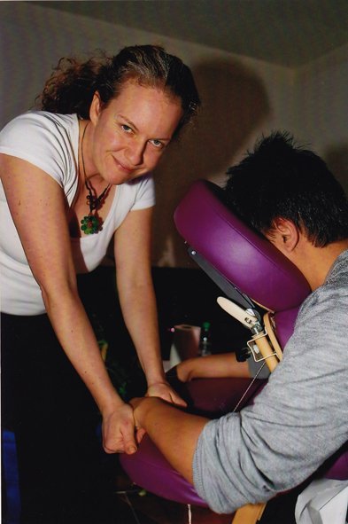 Une praticienne, souriante, masse le bras d'un homme installé sur une chaise de massage violette