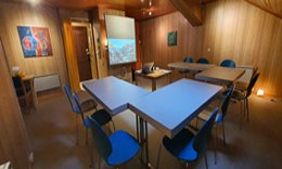 La salle aménagée pour une conférence : tables en U, chaises bleues et écran de projection